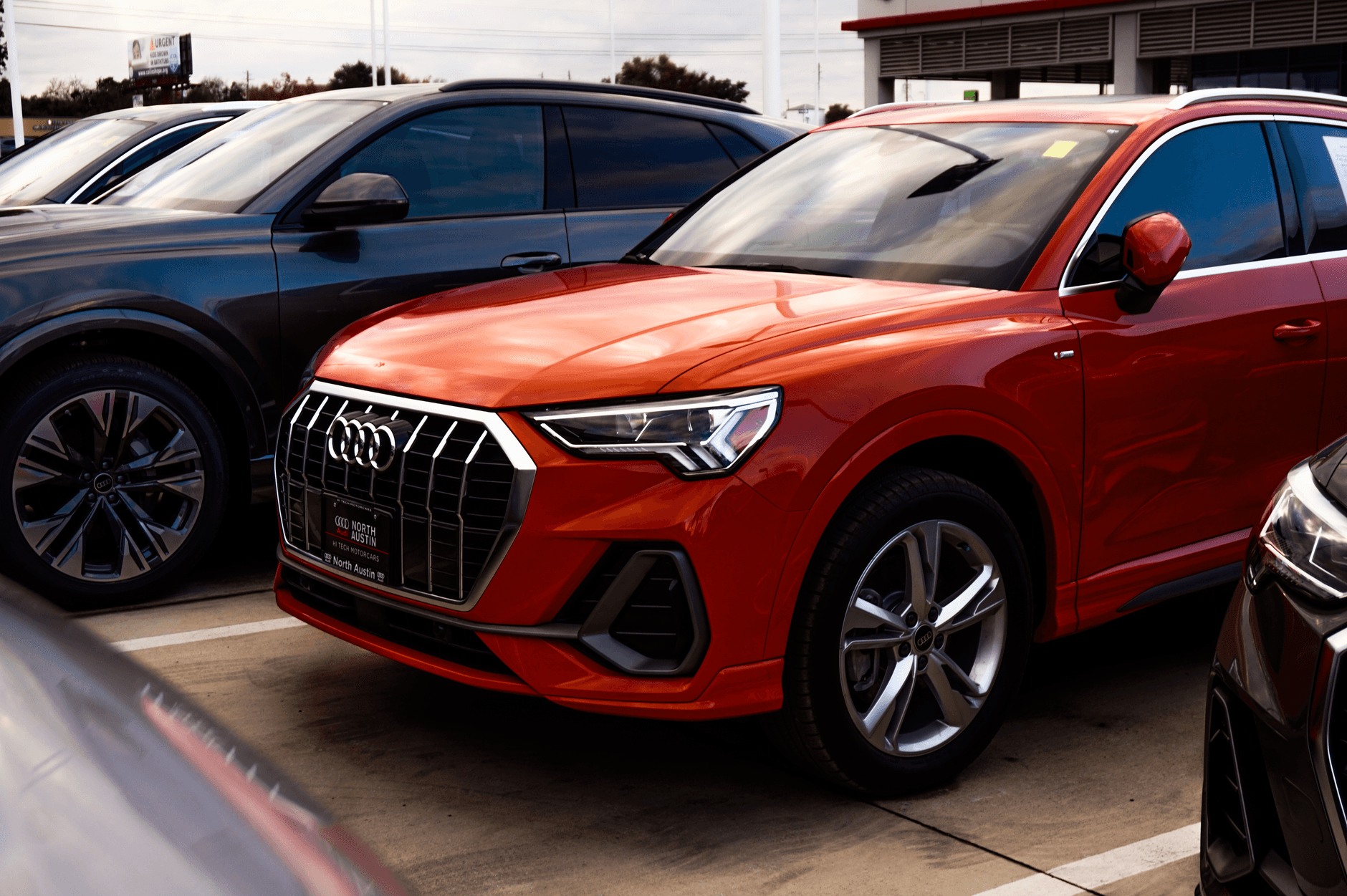 A vibrant orange SUV parked among other vehicles at a car dealership, showcasing modern car design.