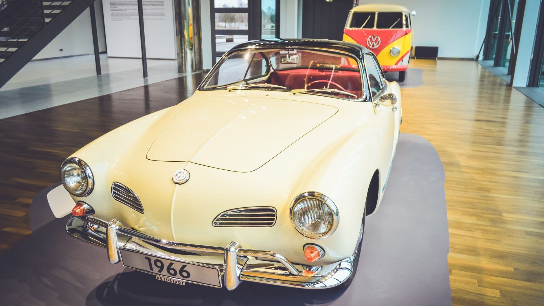 Vintage 1966 Volkswagen on display indoors with Kombi van in background.